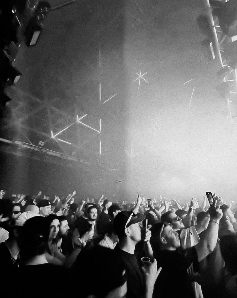 Black and white photo of a crowd raising their hands and phones under stage lights