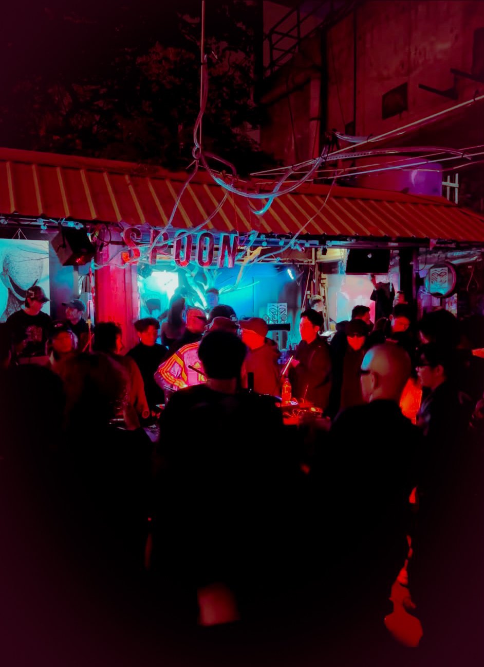 A crowd outside Spoon, a small bar lit red and blue at night
